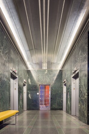 Un moderno vestíbulo de ascensores con paredes de mármol, un banco y un ascensor central con puerta colorida.