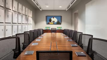 A conference room with a long table, black mesh chairs, and framed pictures on the walls.