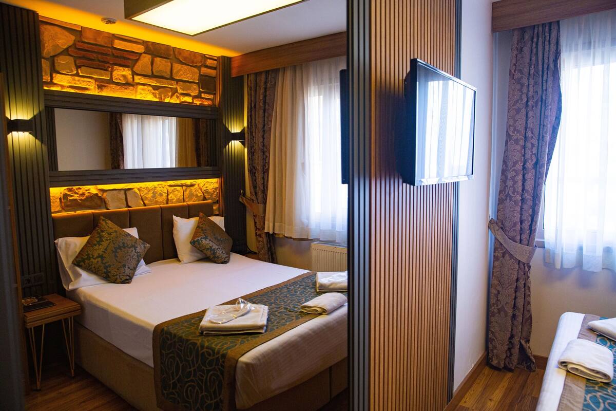 Une chambre d’hôtel avec un grand lit, une télévision, un mur décoratif en pierre et une fenêtre avec des rideaux.