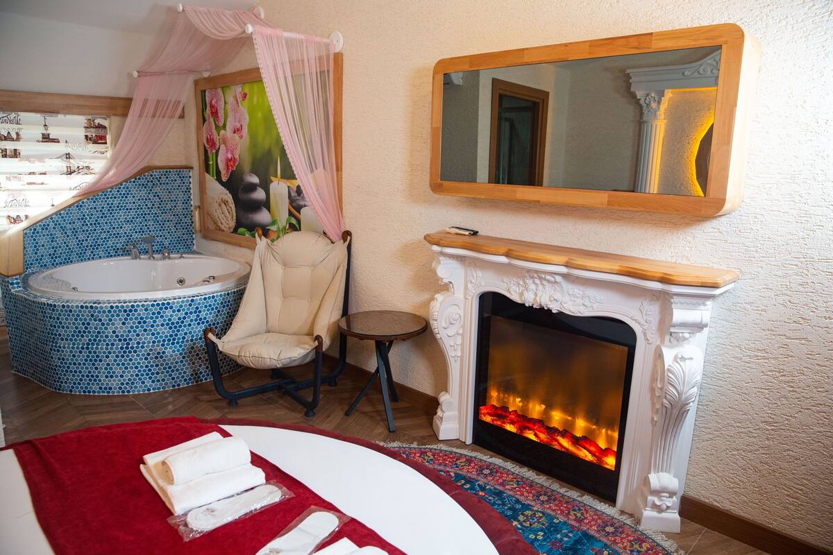 Une salle de bain avec une baignoire, une chaise, une cheminée et un miroir.
