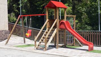 Una struttura giochi in legno con uno scivolo rosso e un’altalena.