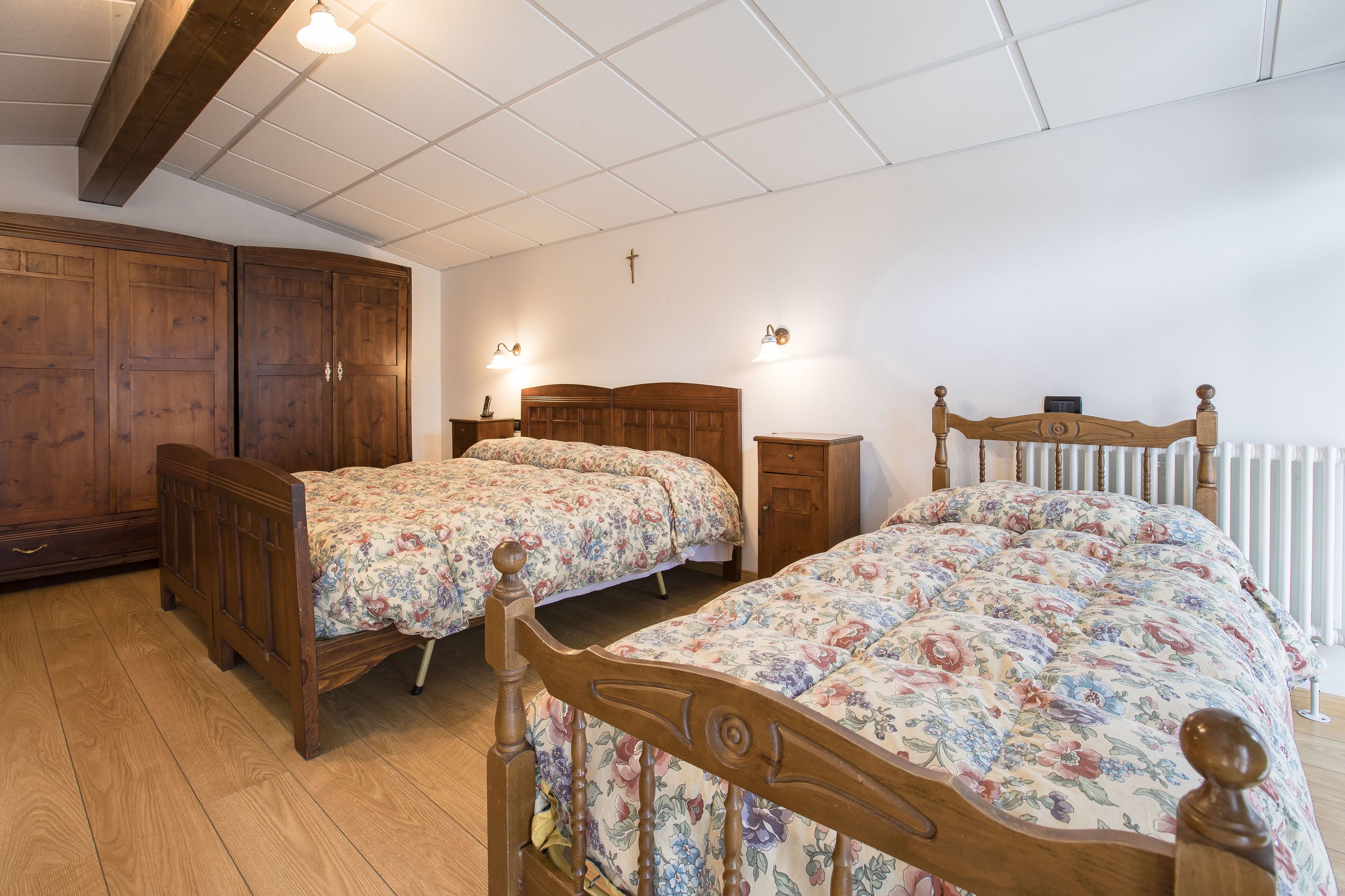 A bedroom with two wooden beds, a wardrobe, and a radiator.