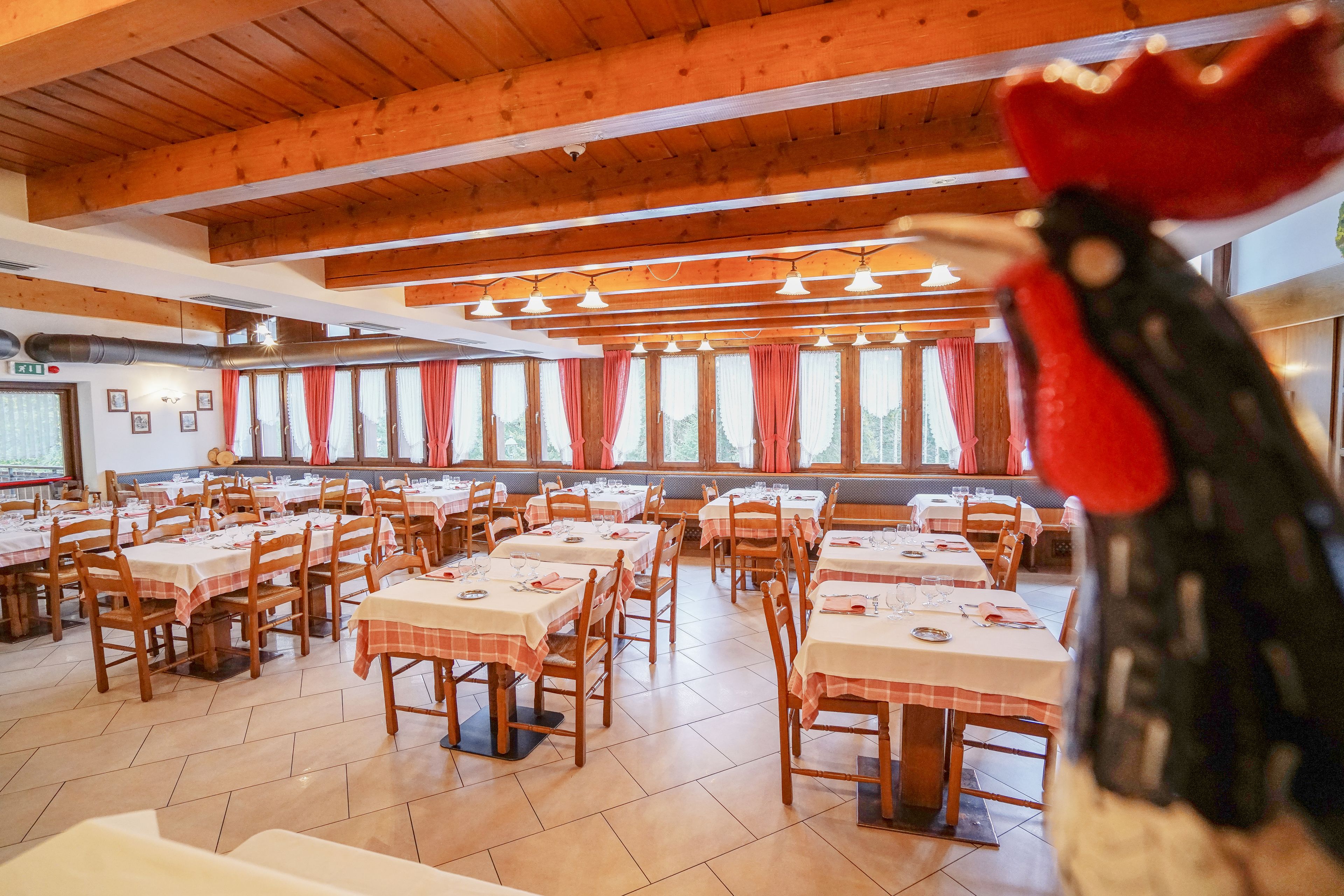 Ein Restaurant mit Holzbalken, mehreren Tischen mit weißen Tischdecken und roten Vorhängen.