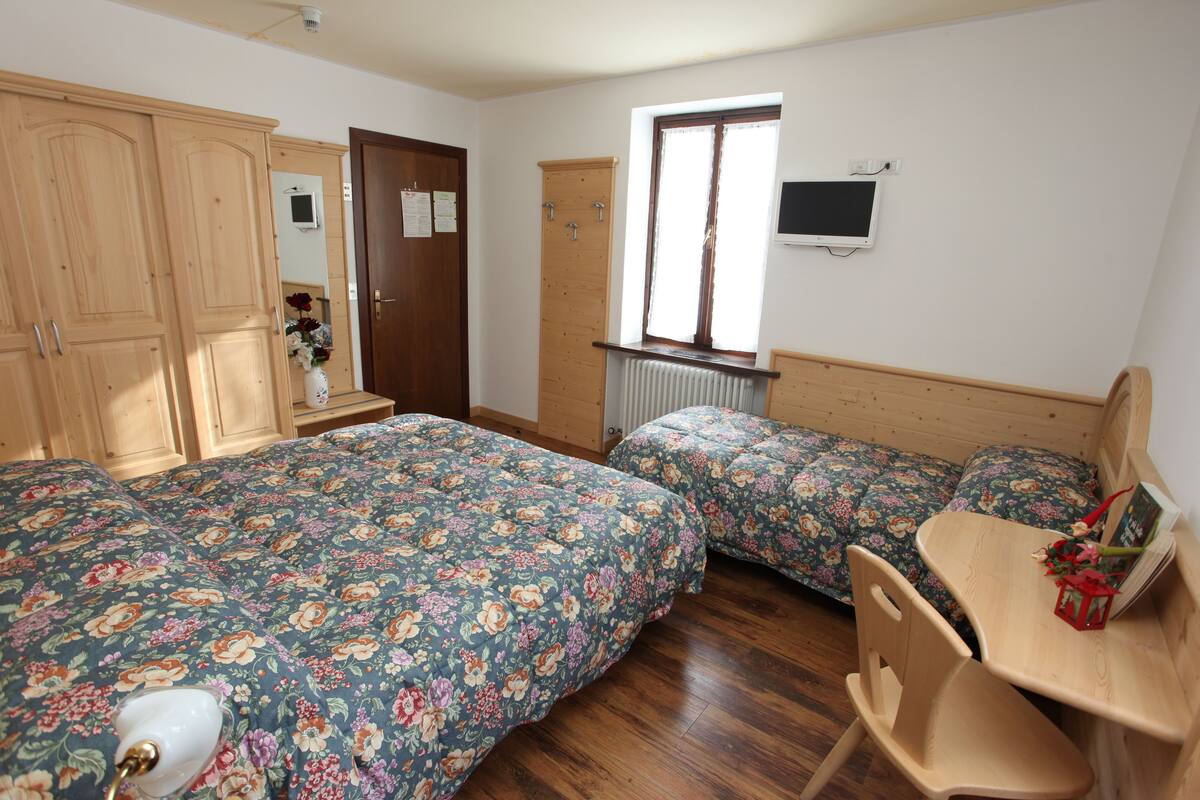 Ein Schlafzimmer mit zwei Betten, einem Holztisch, einem Stuhl, einem Heizkörper, einem Fenster und einem Fernseher an der Wand.