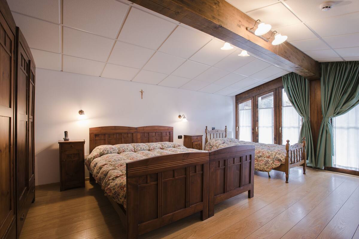 Ein Schlafzimmer mit zwei Holzbetten, einem Holzschrank, einem Nachttisch und einem Fenster mit Vorhängen.
