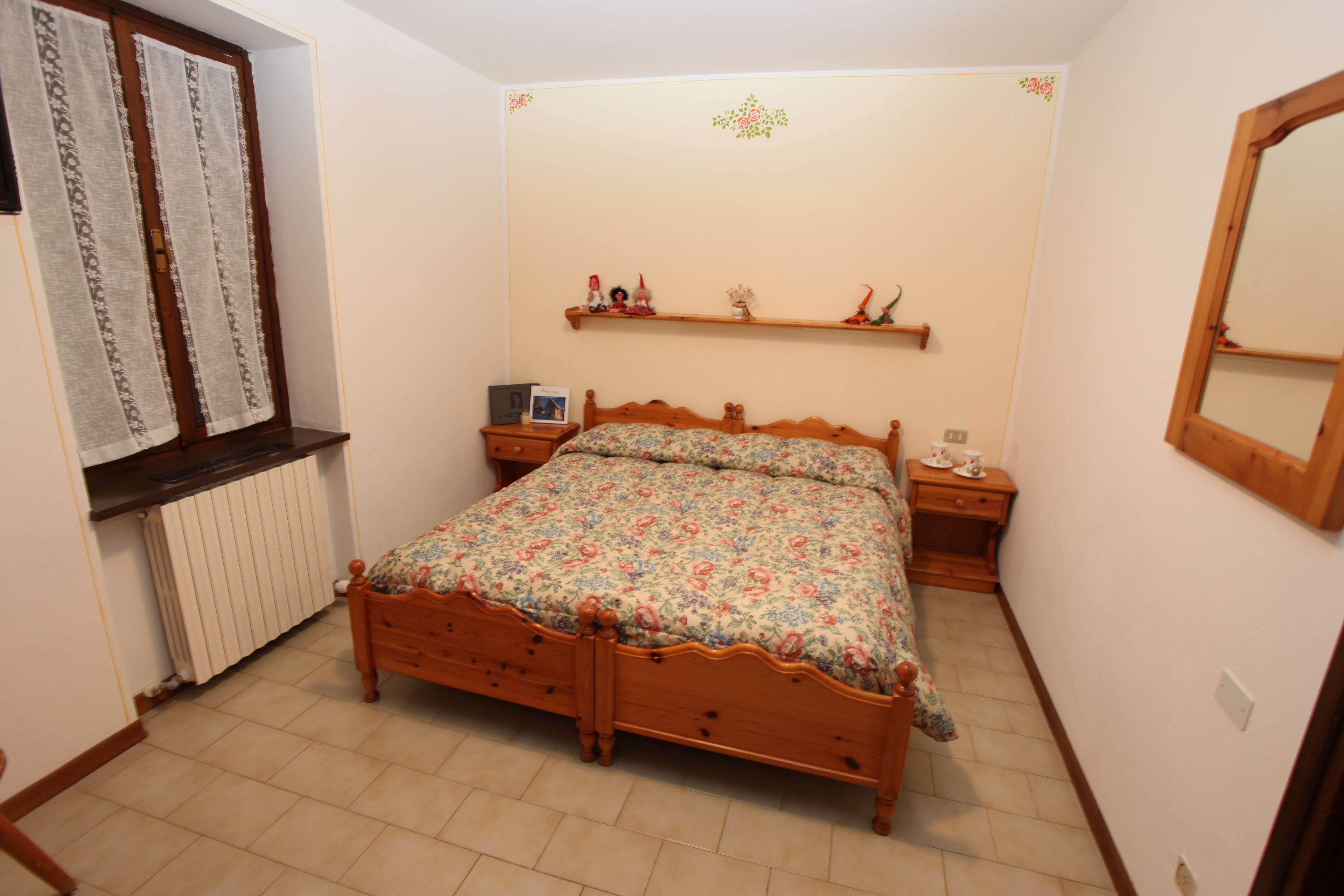 Un dormitorio con cama de madera, una mesita de noche, un aparador, un radiador y una estantería con objetos decorativos.