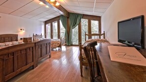 Une chambre d’hôtel avec un lit en bois, un bureau en bois, une télévision et de grandes fenêtres avec des rideaux.