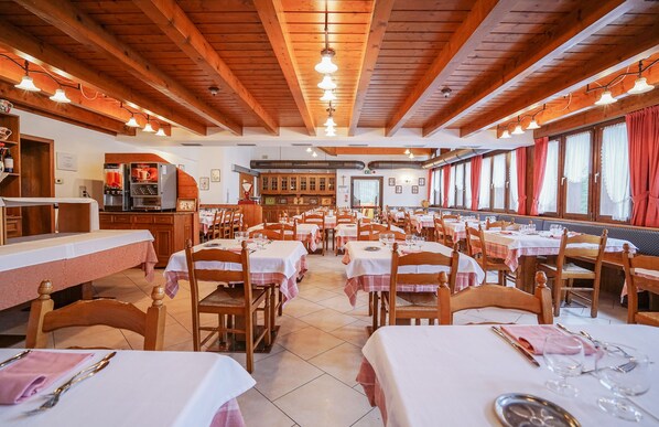 A restaurant with wooden beams, white tables, and red curtains.