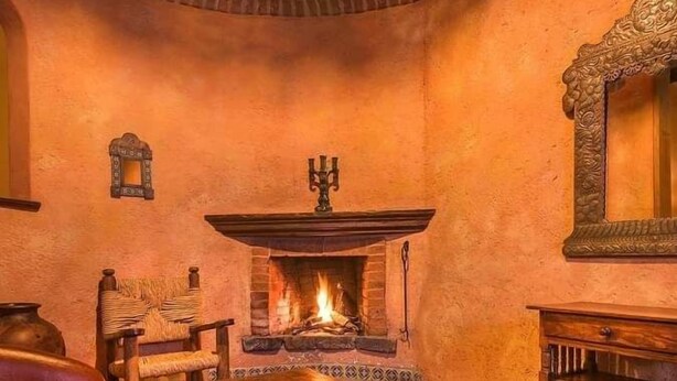 A cozy room with a fireplace, a wooden table, a chair, and a mirror on the wall.