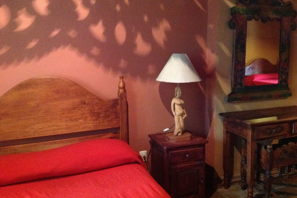 Une chambre à coucher avec une tête de lit en bois, une lampe de chevet, un miroir et une couverture de lit rouge.