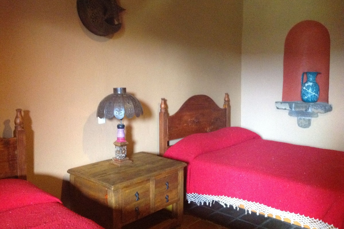 Une chambre avec deux lits, une table de chevet en bois, une lampe et une étagère murale ornée d’un vase.
