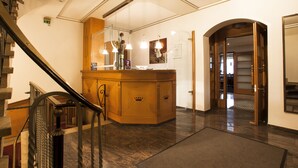 Eine Hotelhalle mit einem Holzbüro, einer Treppe und Blick ins Innere durch einen Rundbogen.