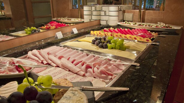 Ein reichhaltiges Buffet mit verschiedenen Speisen, darunter Fleisch, Käse, Obst und Gemüse.