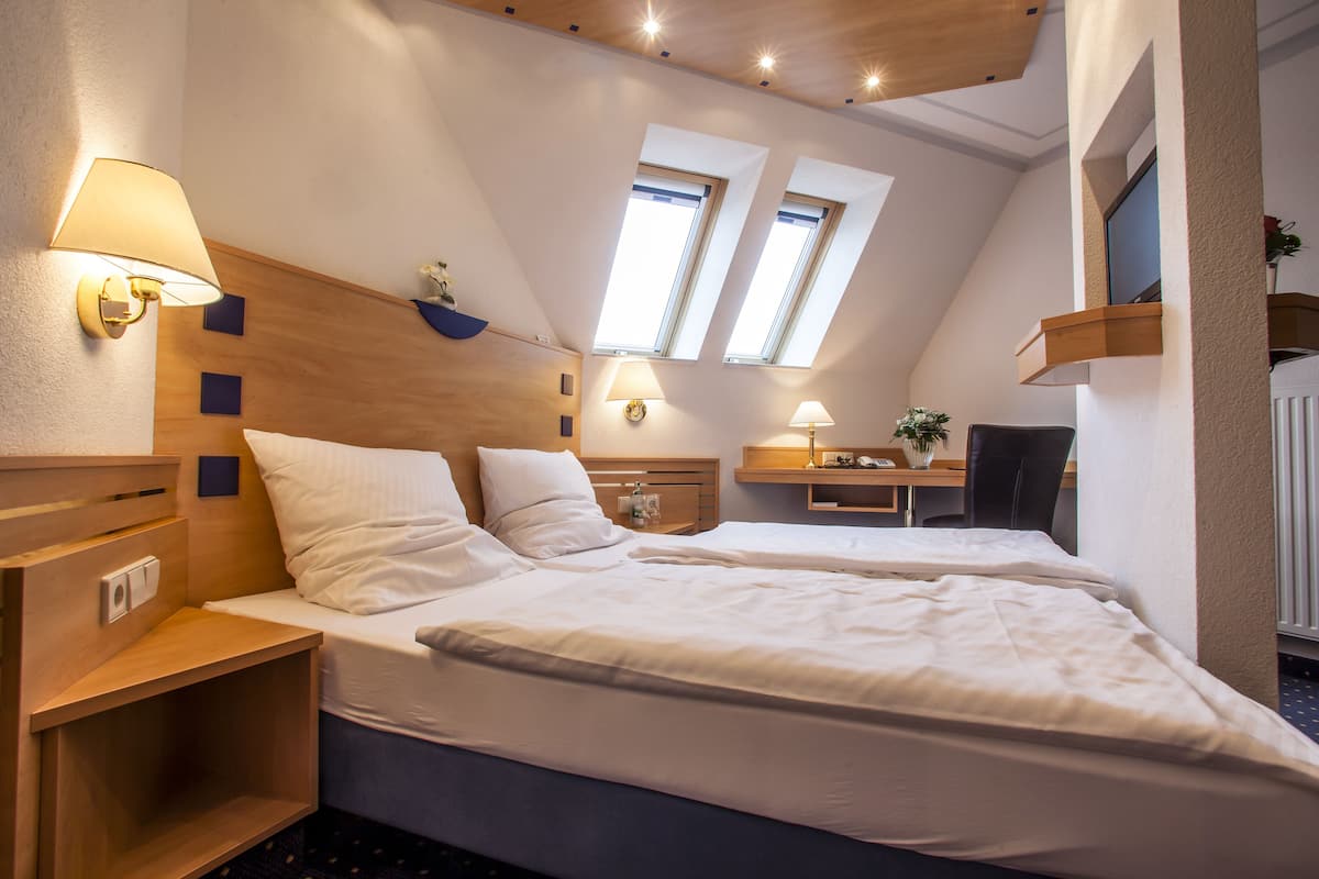 Une chambre d’hôtel avec deux lits, un bureau, une chaise et deux fenêtres.