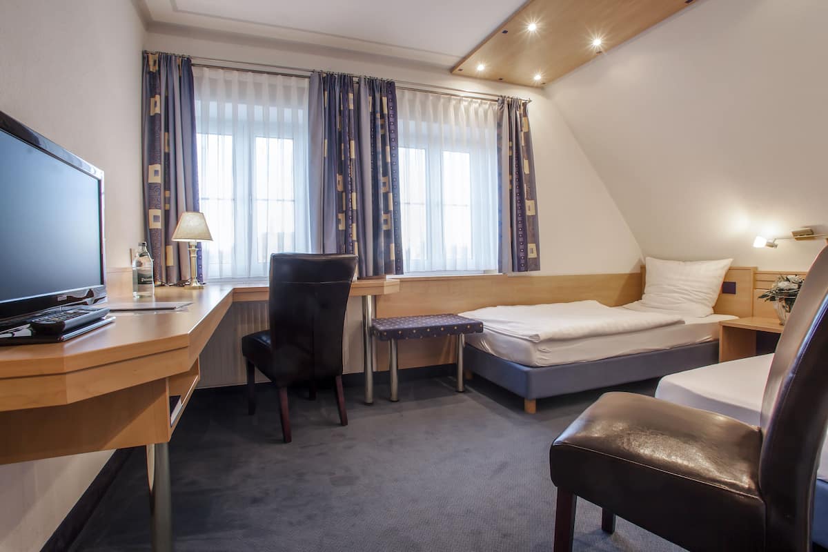 Une chambre d’hôtel équipée d’un bureau, d’une chaise, d’un lit, d’une télévision et d’une fenêtre avec des rideaux.