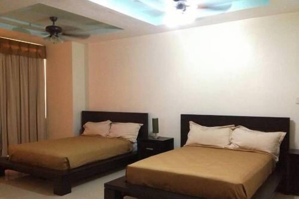A hotel room with two single beds, a ceiling fan, and a window with curtains.