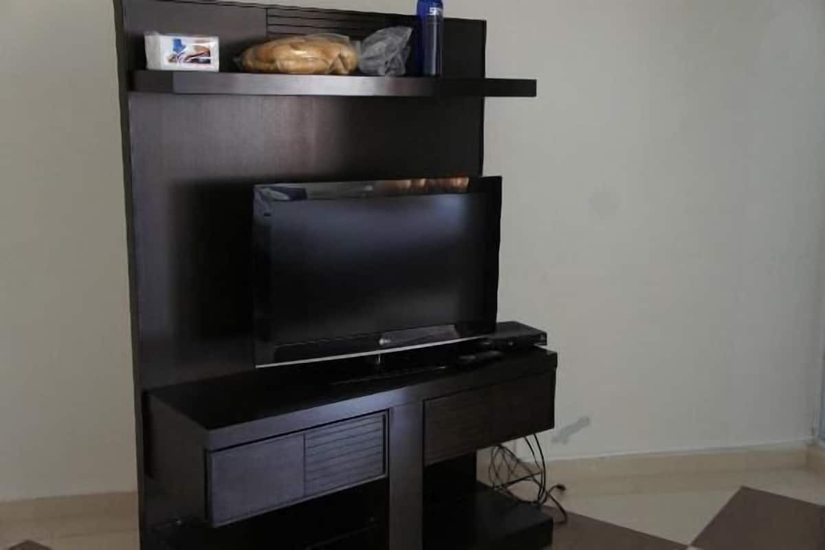 A black entertainment unit with a flat-screen TV, a shelf with a loaf of bread and a bottle, and a drawer below.