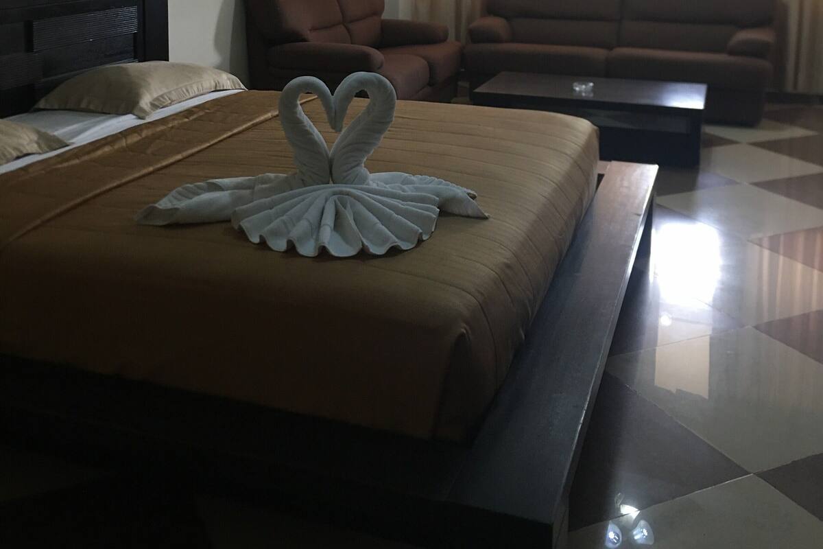 A hotel room with a bed, a sofa, a coffee table, and a painting on the wall.