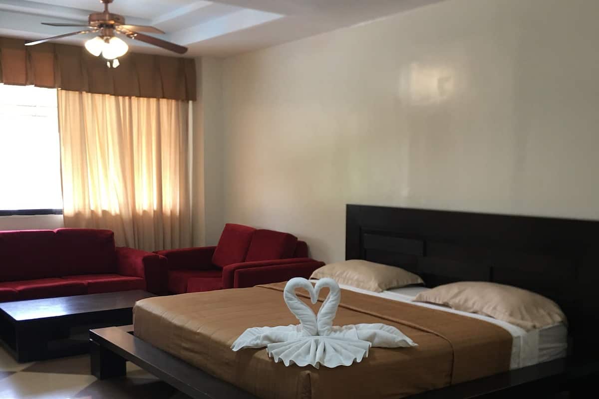 A hotel room with a bed, a red sofa, a ceiling fan, and a checkered floor.