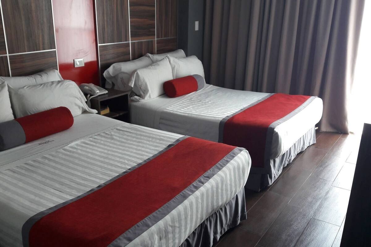 Two beds with red and gray bedding, a nightstand with a phone, and a wooden headboard.