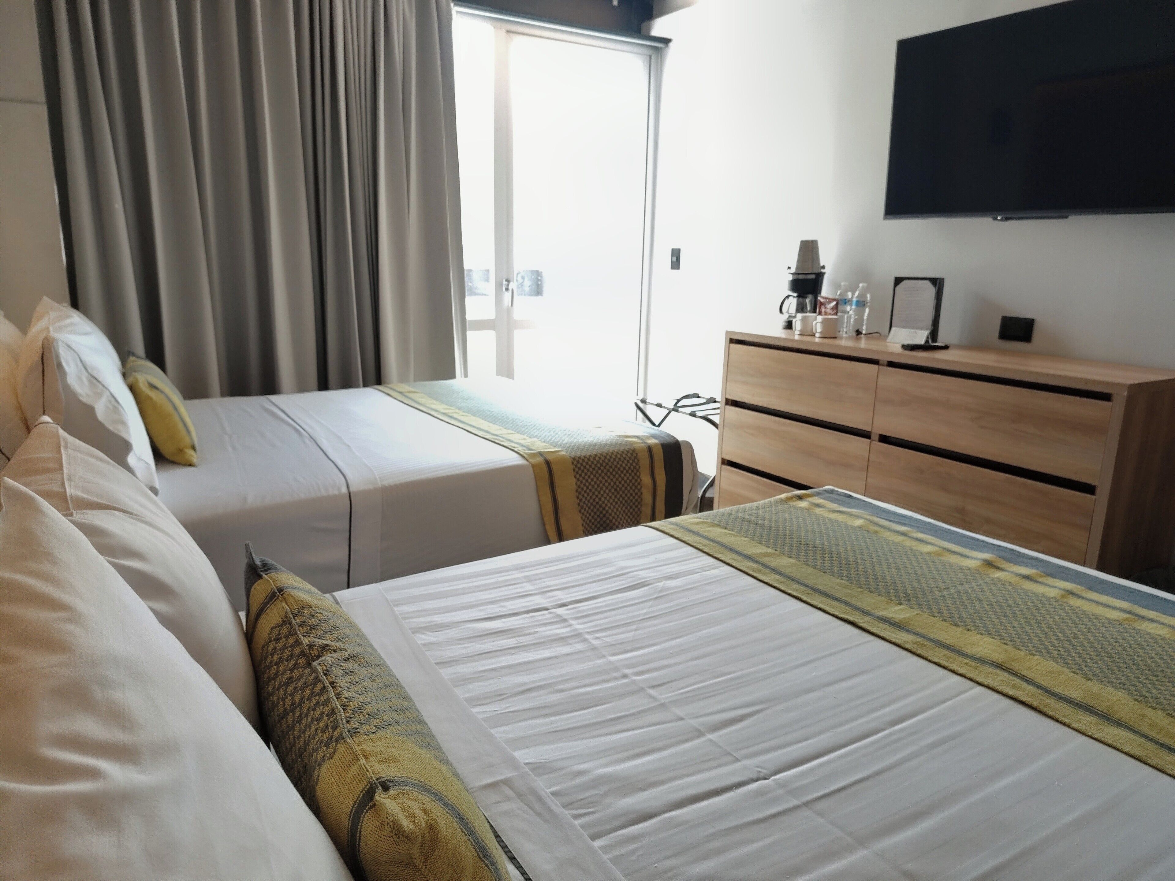 Une chambre d’hôtel avec deux lits, une commode en bois, un téléviseur à écran plat et une fenêtre avec des rideaux.