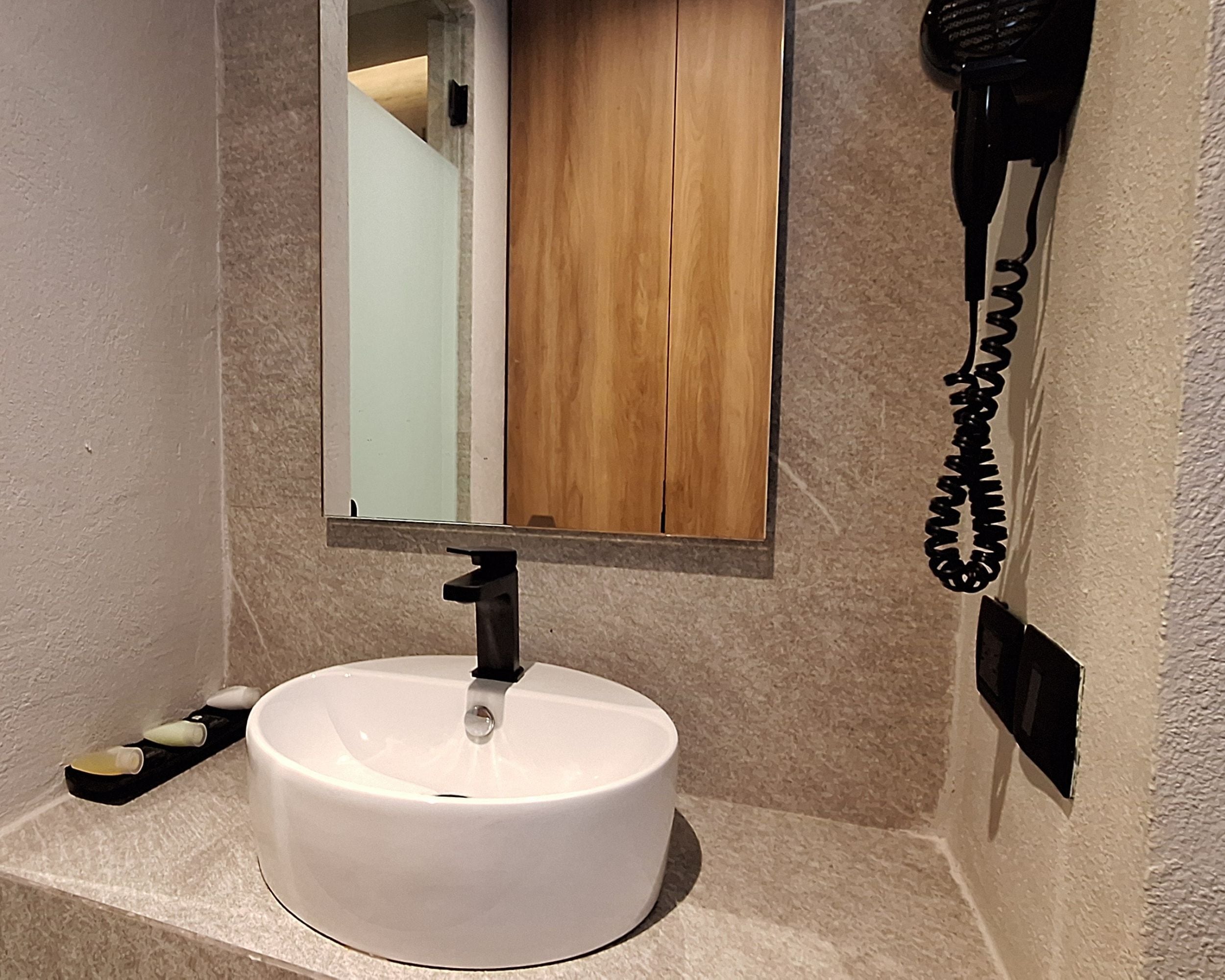 A bathroom with a white sink, a mirror, and a hairdryer mounted on the wall.