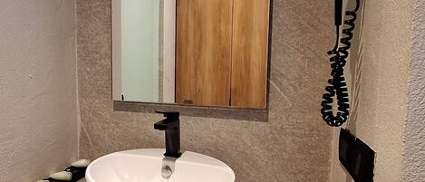 A bathroom with a white sink, a mirror, and a hairdryer mounted on the wall.