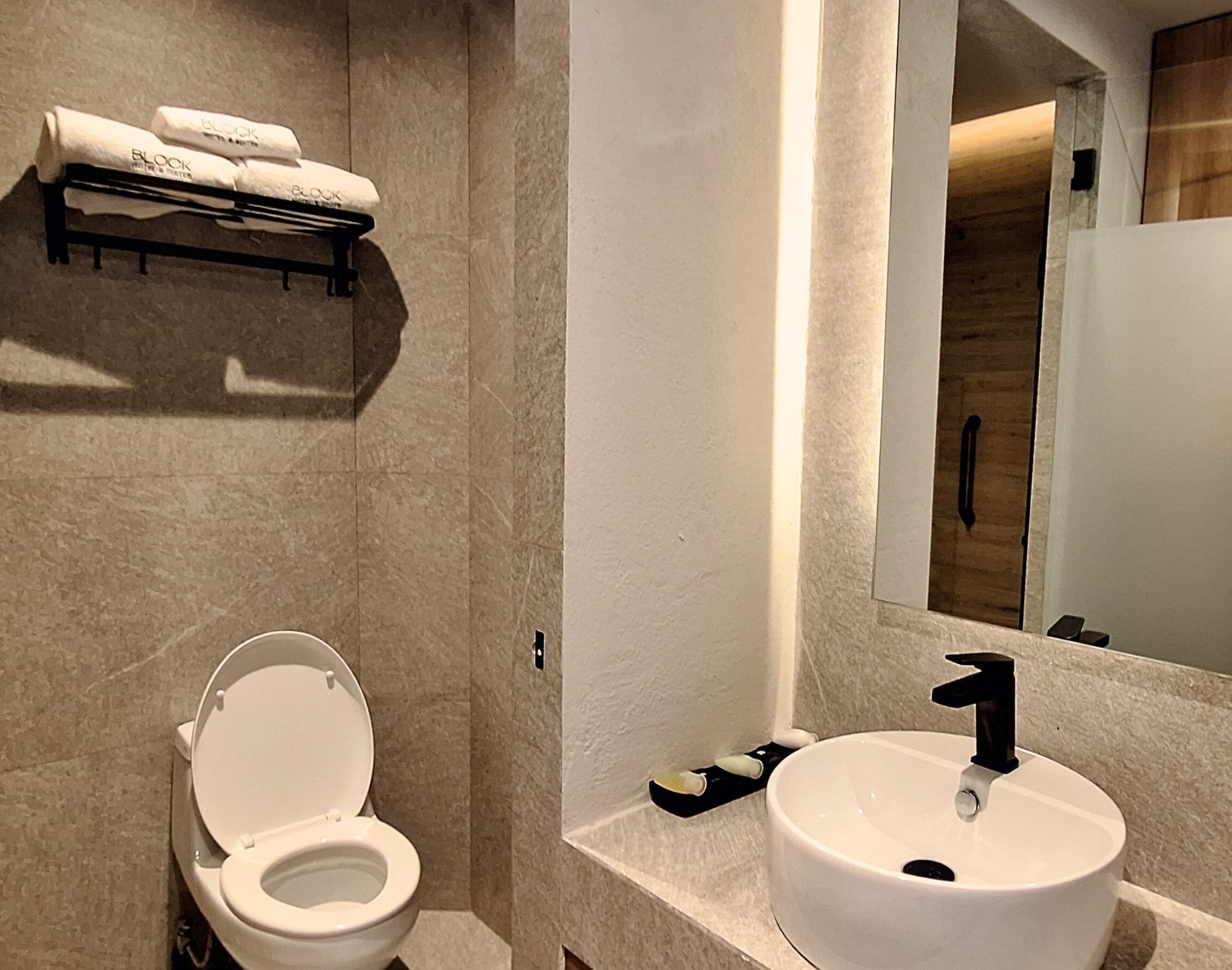 Un baño moderno con inodoro blanco, lavamanos con grifo negro y toallero con toallas.
