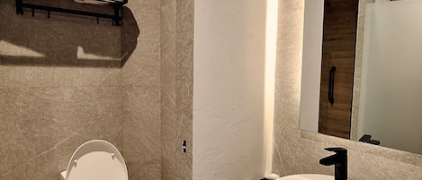 Un baño moderno con inodoro blanco, lavamanos con grifo negro y toallero con toallas.