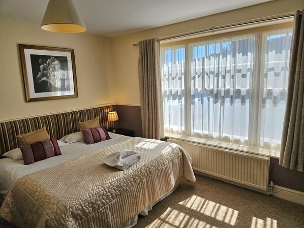 A hotel room with a large bed, a bedside table with a lamp, a framed picture on the wall, and a window with curtains. - Simonsbath House (Minehead)