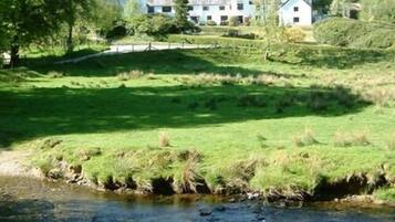 A grassy area with a small stream and white buildings in the background.