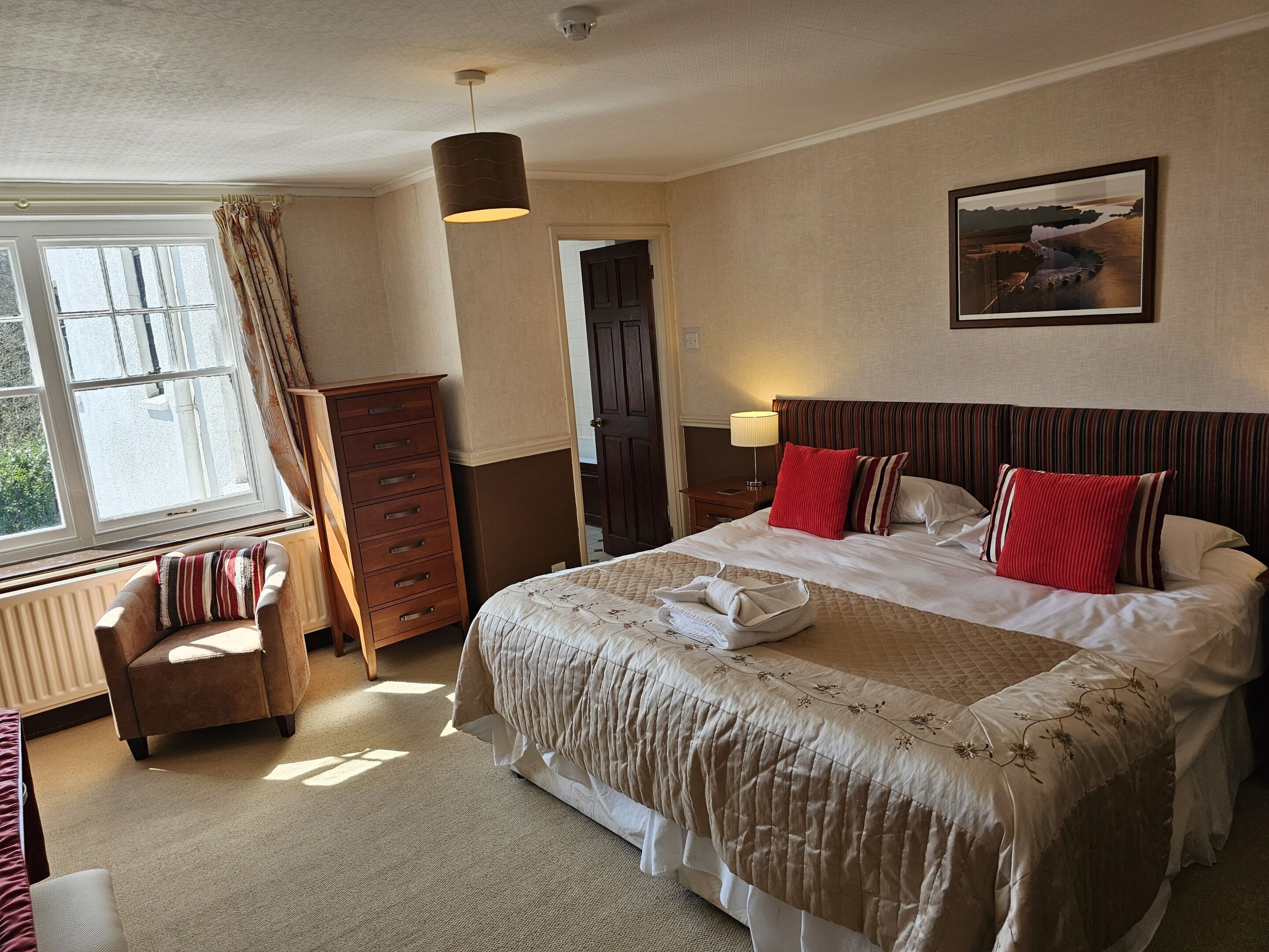 A hotel room with a large bed, a wooden dresser, a chair, and a window with curtains.