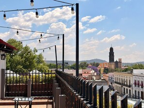 Un balcón con vista a un paisaje urbano, que incluye una imponente torre de iglesia.