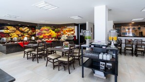 A restaurant with multiple dining tables and chairs, a buffet area with food displays, and a juice dispenser. - Sleep Inn Puebla Centro Histórico (Puebla)