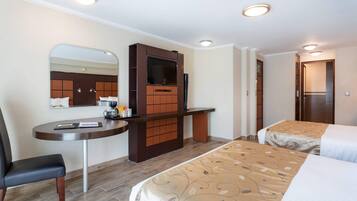 A hotel room with a desk, two beds, a television, and a mirror.