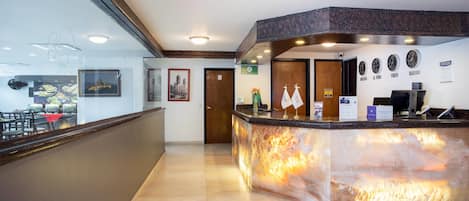 A hotel reception area with a marble counter, framed pictures on the wall, and clocks displaying different cities.