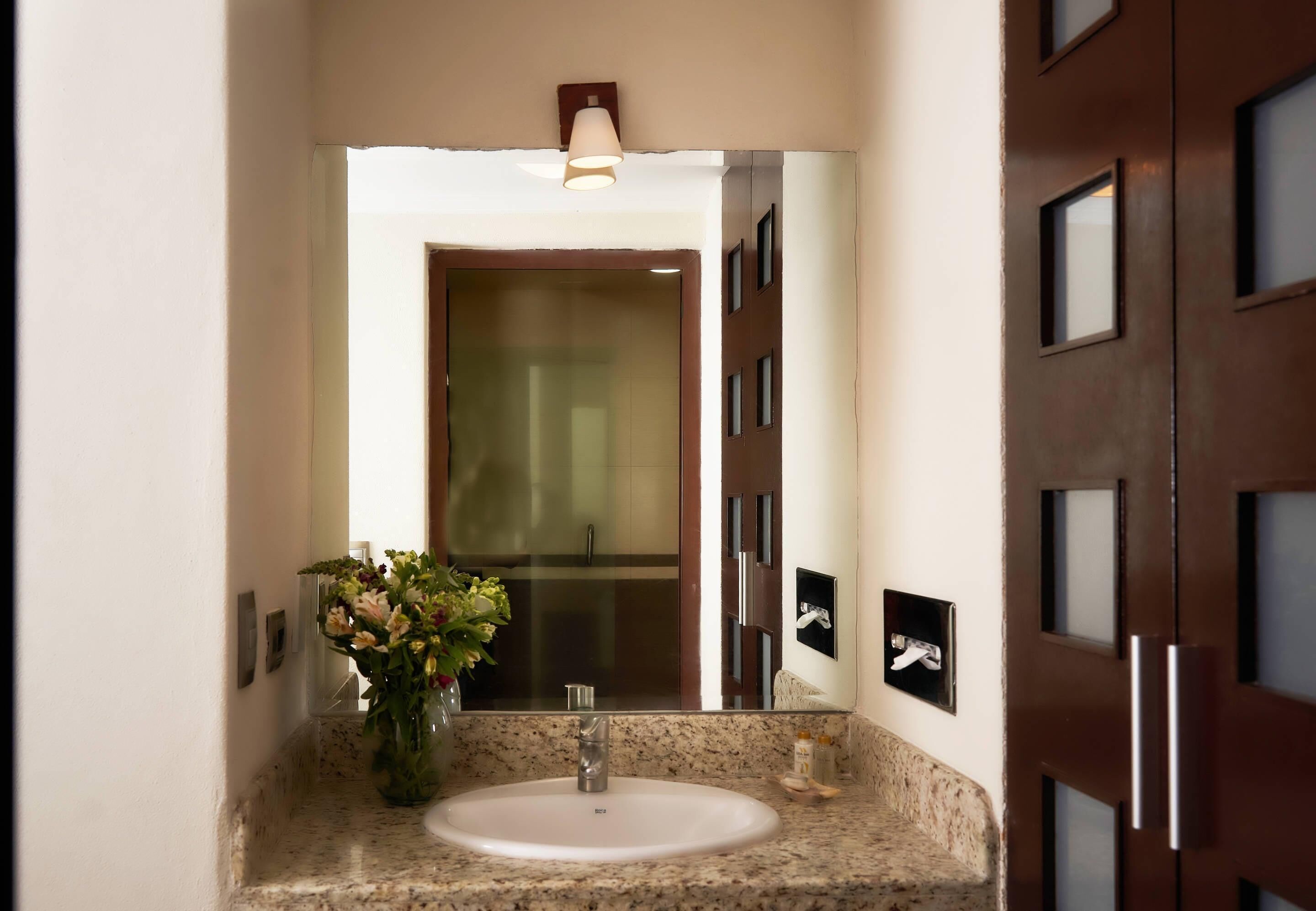 A bathroom with a sink, mirror, and a vase of flowers.