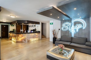 A hotel lobby with a reception desk, a sofa, a glass coffee table, and a neon sign.