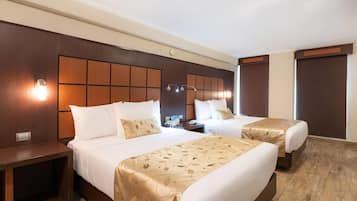 A hotel room with two beds, wooden headboards, and bedside lamps.