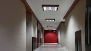 A long, narrow hallway with a red wall at the end, recessed lighting, and a green emergency exit sign. - Sleep Inn Puebla Centro Histórico (Puebla)