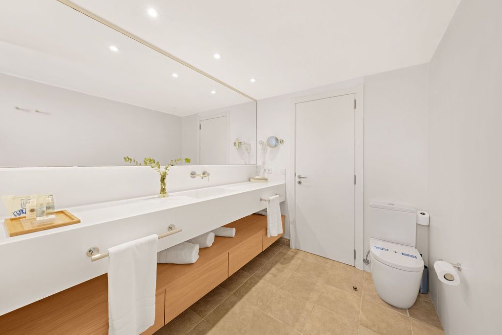 Un baño moderno con un espejo grande, sanitarios blancos y un tocador de madera.