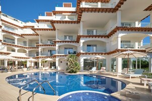 Un hotel de varios pisos con una piscina central rodeada de tumbonas y sombrillas.