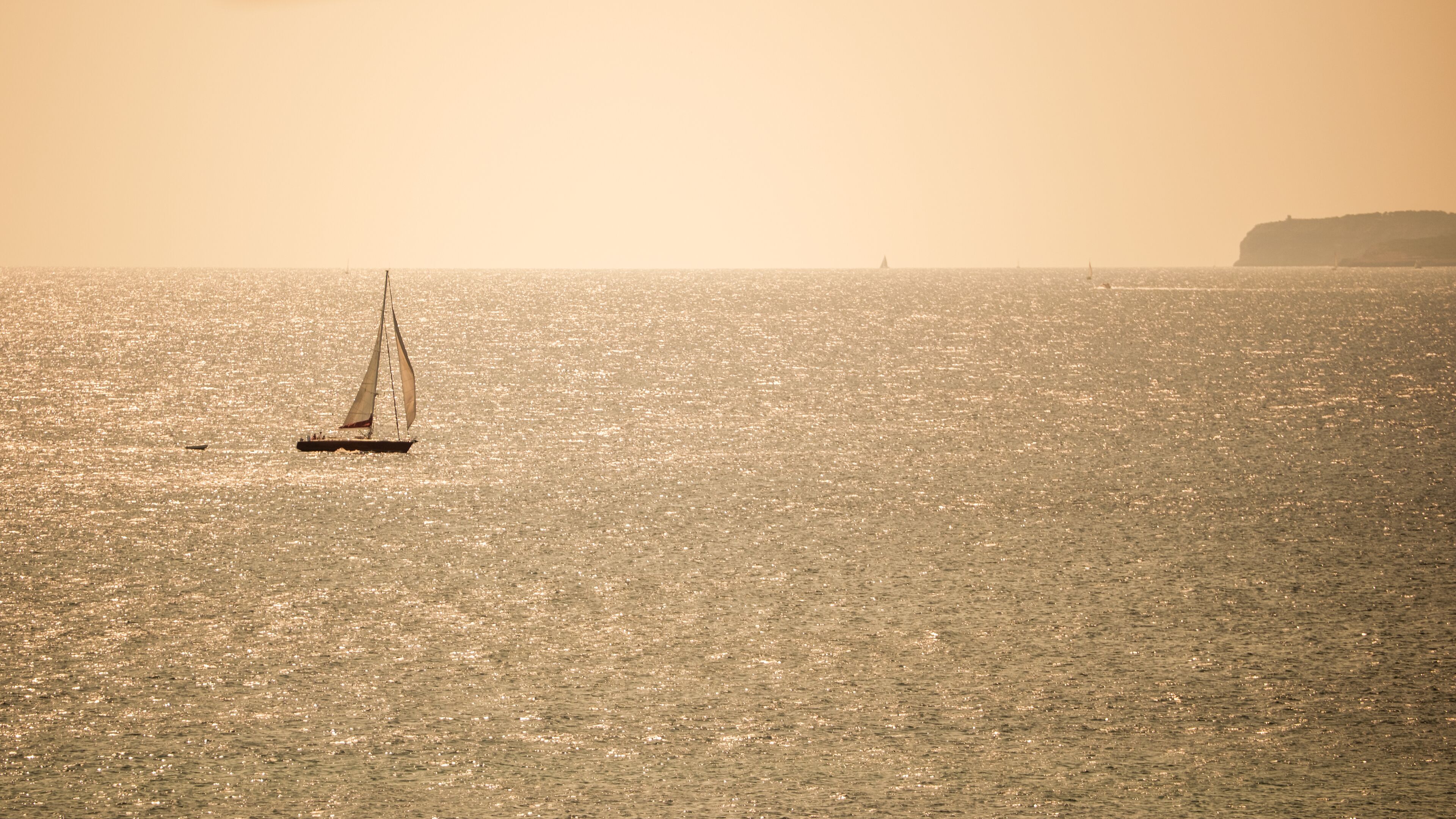 Un velero en un mar tranquilo con tierra a lo lejos.