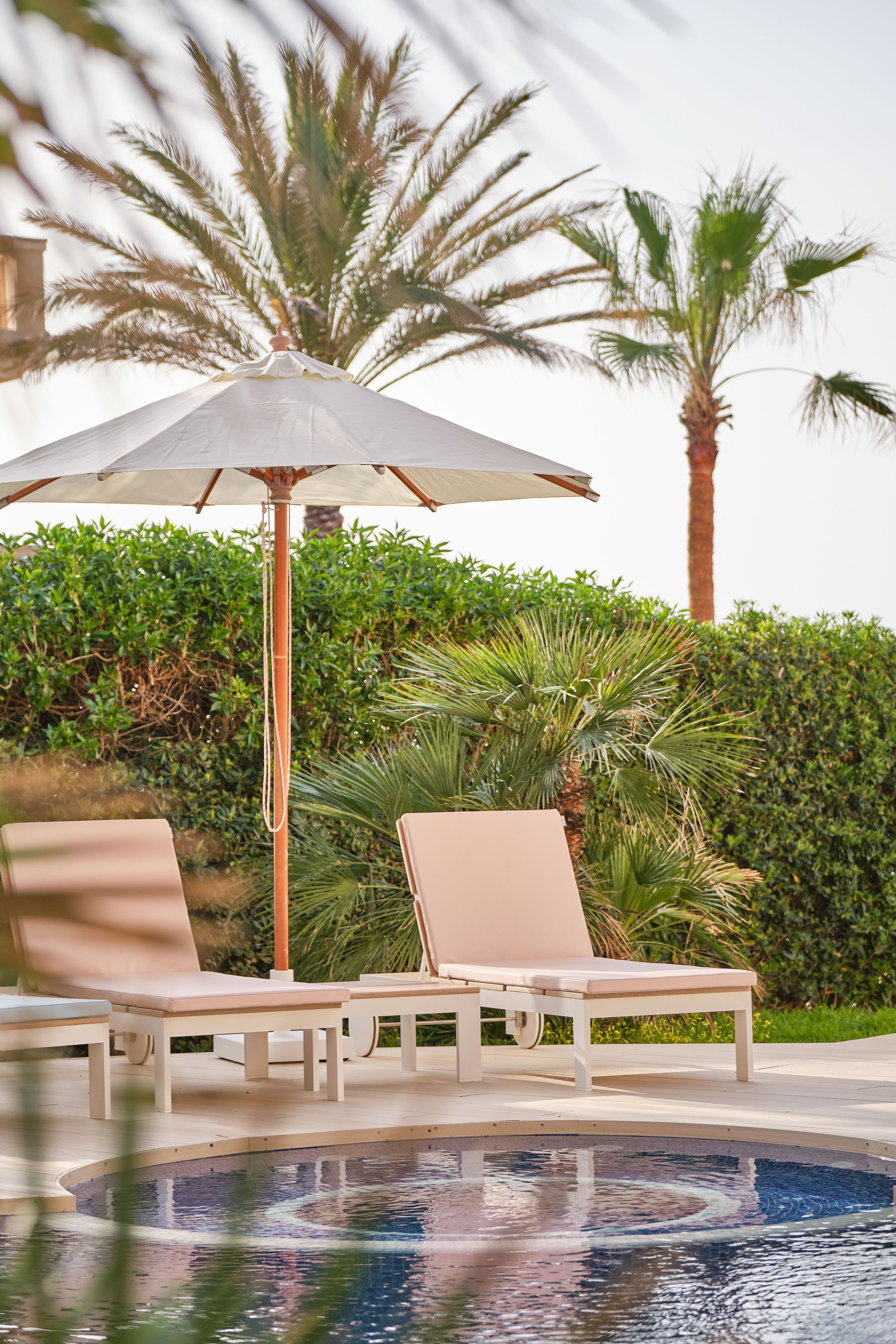 Zona junto a la piscina con sillones de descanso y una sombrilla.