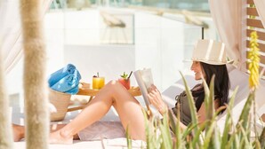 Una persona relajándose en una tumbona con una bebida y un libro, rodeada de follaje.
