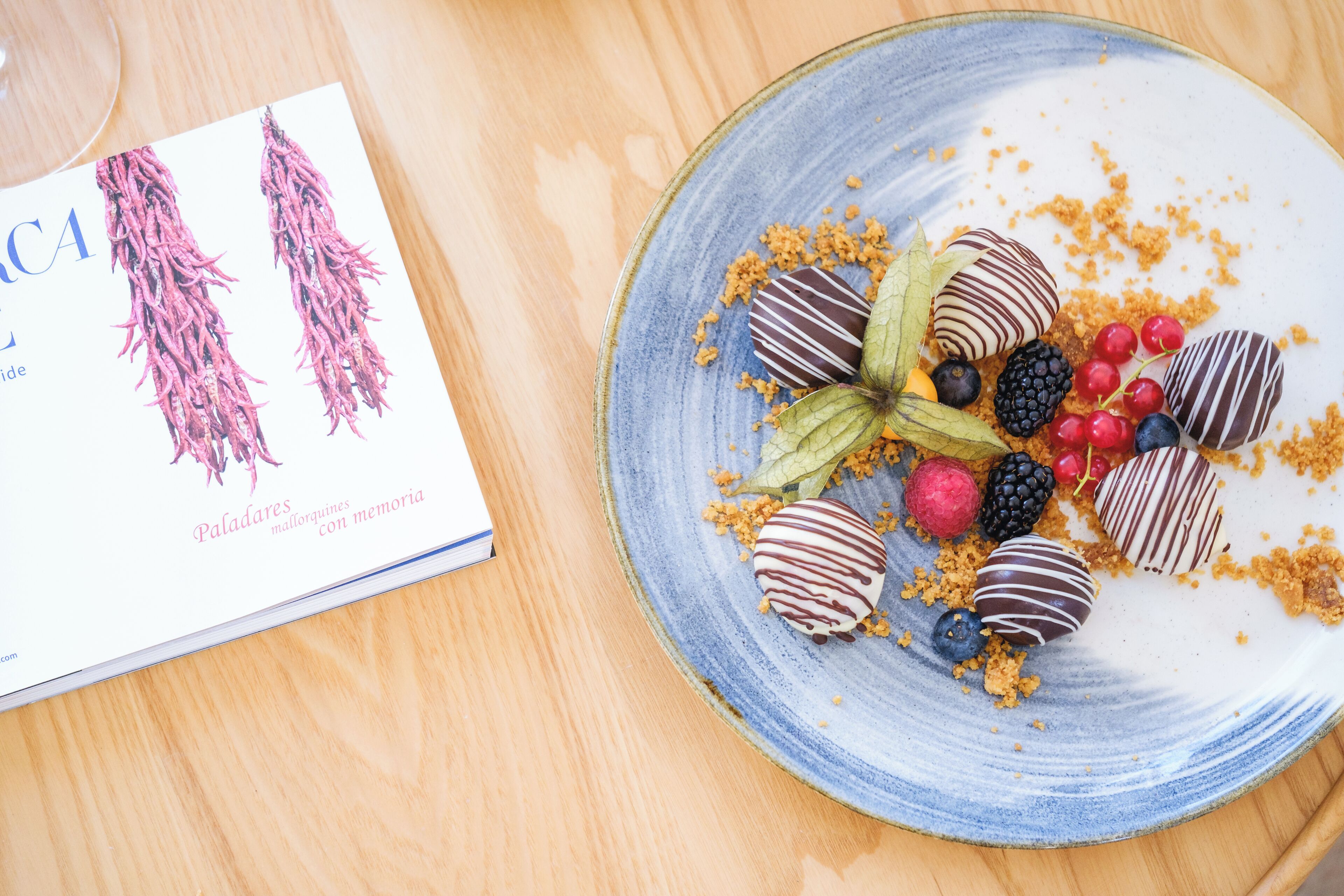 Ein Teller mit schokoladenüberzogenen Erdbeeren und Beeren, neben dem ein Buch liegt.