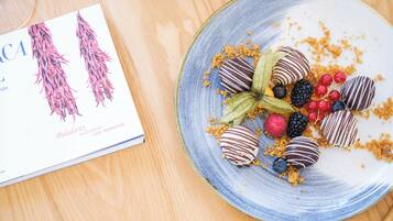 Un plato de fresas cubiertas de chocolate y bayas, con un libro a un lado.