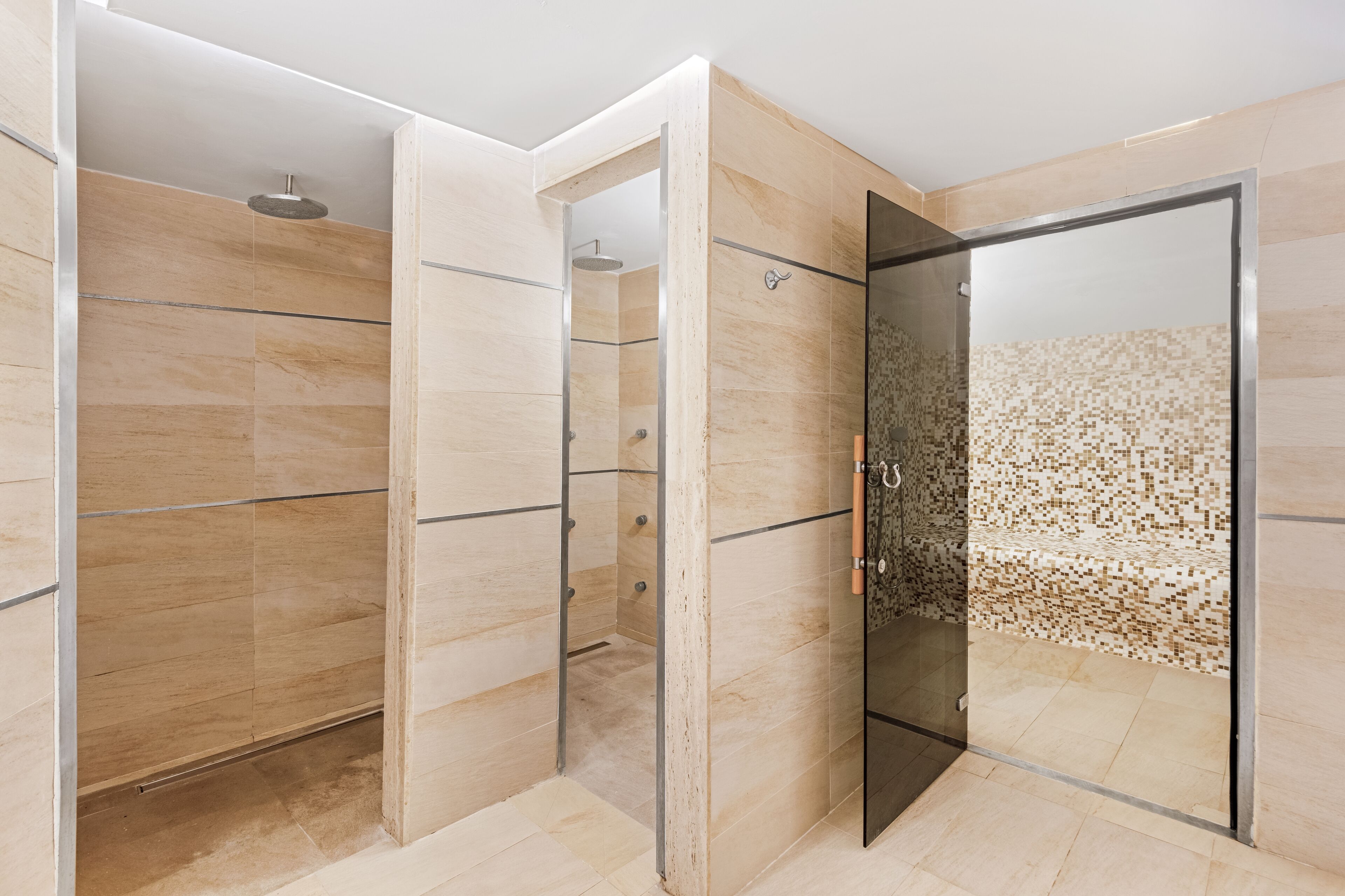 Un baño moderno con cabina de ducha de vidrio, paredes con azulejos color beige y un cabezal de ducha.