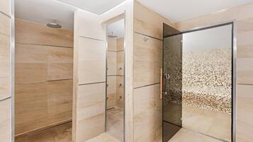 Un baño moderno con cabina de ducha de vidrio, paredes con azulejos color beige y un cabezal de ducha.