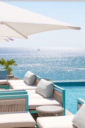 A poolside area with lounge chairs and a table, overlooking a clear blue sea with a sailboat in the distance. - Hotel Villa Chiquita - Adults only (+12) (Ses Salines)